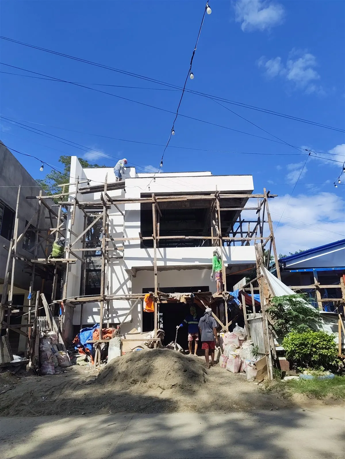 AEDO Construction design-build project nearing completion — full crew finishing exterior work on a 2-storey building in the Philippines