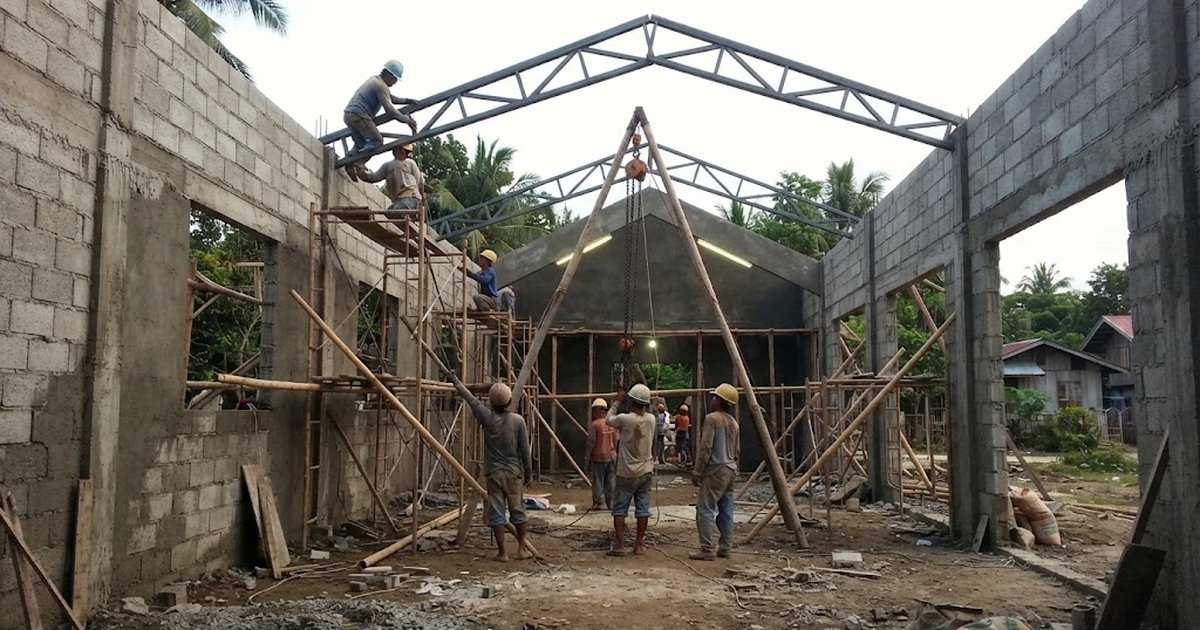 Workers lifting steel roof trusses onto a chapel under construction