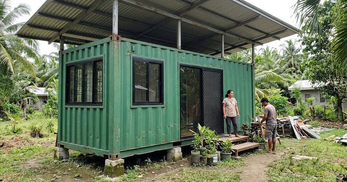 Green shipping container converted into a small house with windows and a roof shade