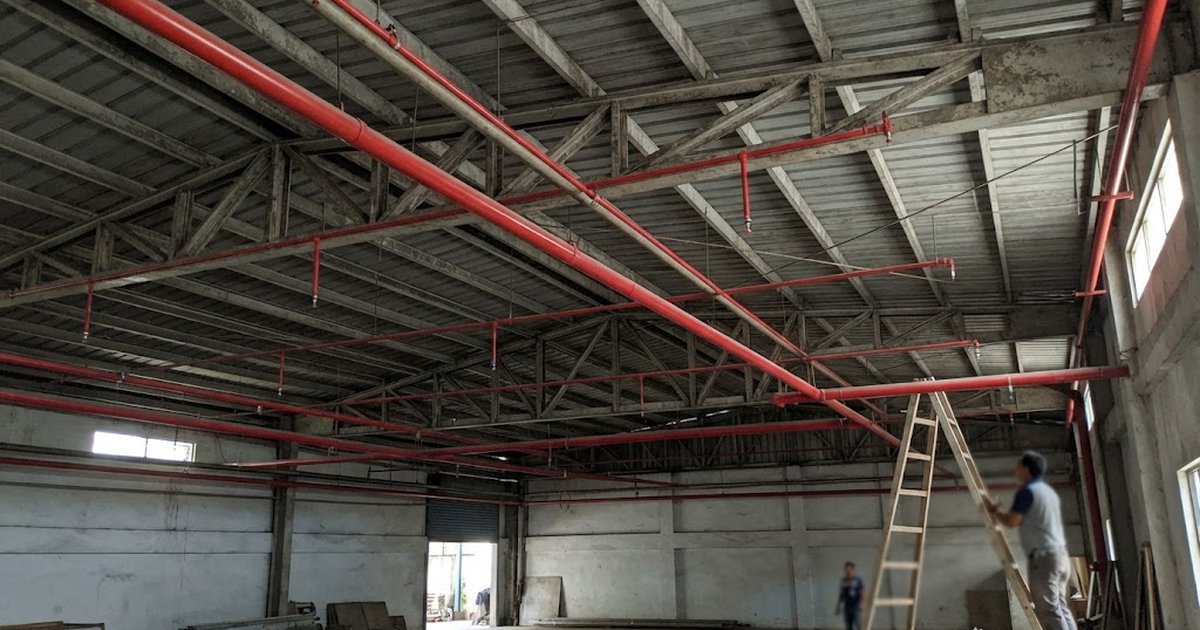 Red fire sprinkler pipes and pendant heads installed under the steel roof framing of a commercial building in the Philippines