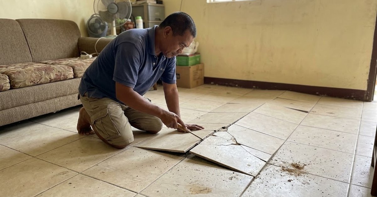 Man checking floor tiles that have popped up and cracked in a living room