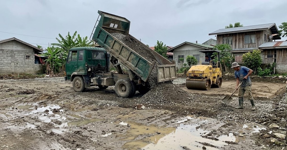 Dump truck unloading fill material on a lot while a roller compacts the ground