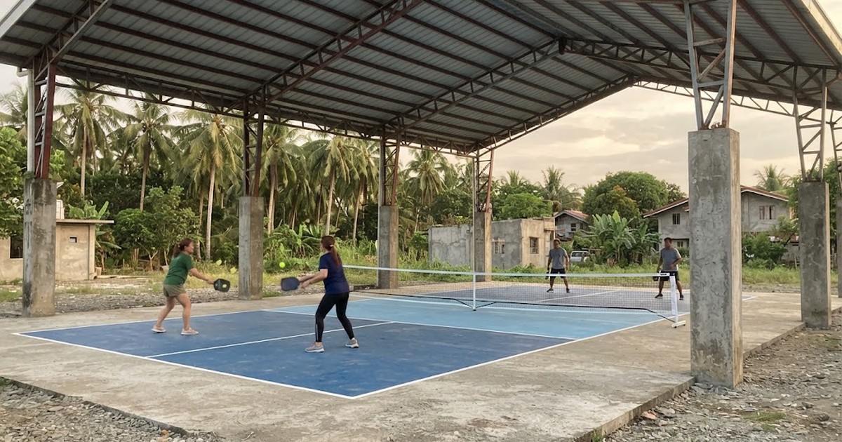 Steel truss roof over two outdoor pickleball courts in the Philippines, late afternoon light, blue court surface