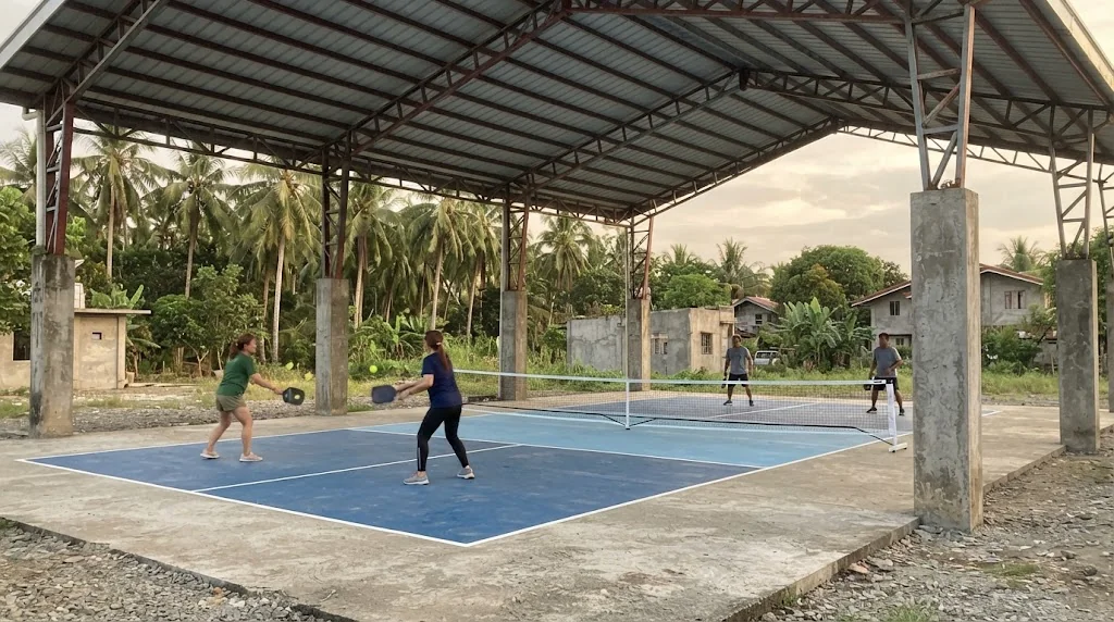 Steel truss roof over two outdoor pickleball courts in the Philippines, late afternoon light, blue court surface