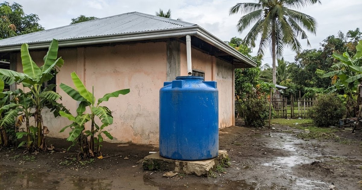 Blue water tank fed by a roof downspout beside a rural house in the Philippines