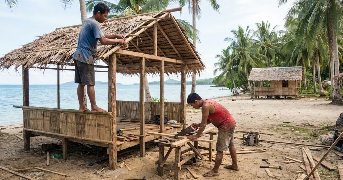 Two Filipino carpenters building a native bamboo and nipa beach cottage on a sandy resort beach