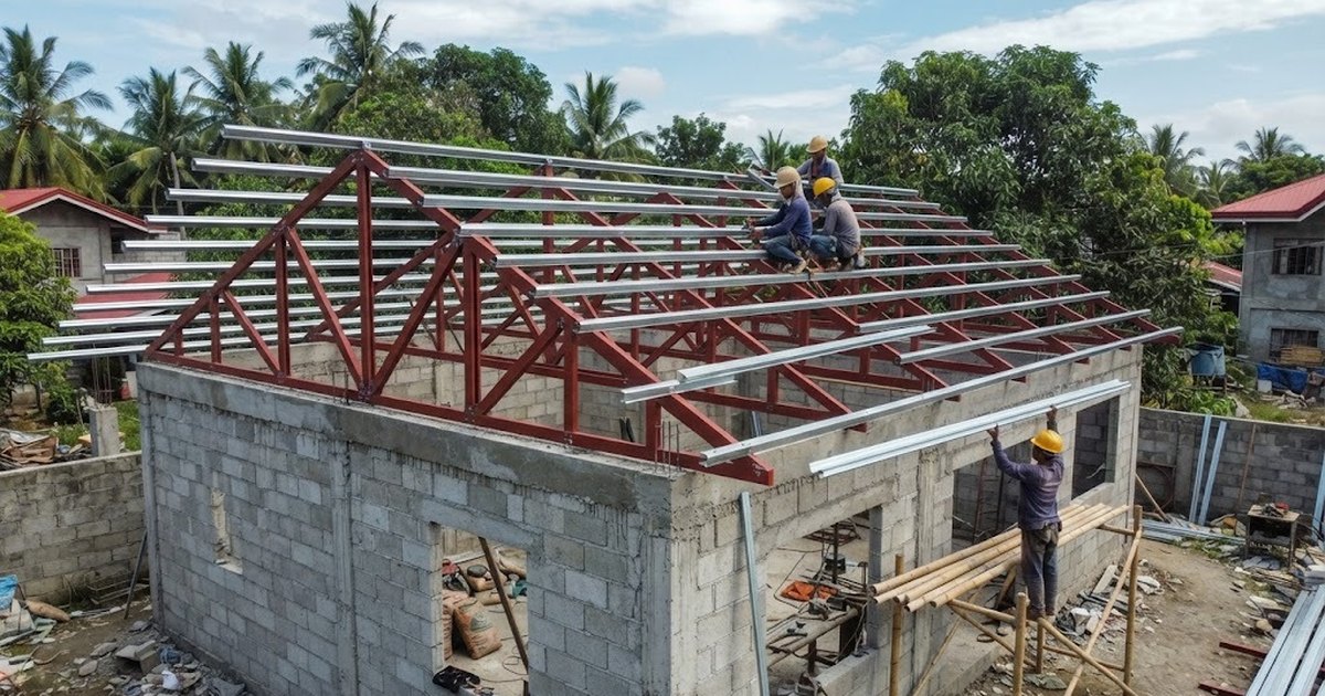 Workers fixing steel purlins on angle-bar roof trusses