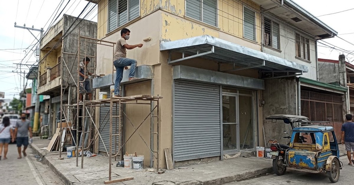Shophouse storefront in the Philippines with workers on scaffolding repainting the front and installing a new metal canopy