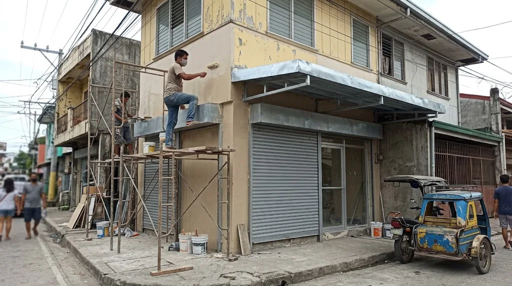 Shophouse storefront in the Philippines with workers on scaffolding repainting the front and installing a new metal canopy