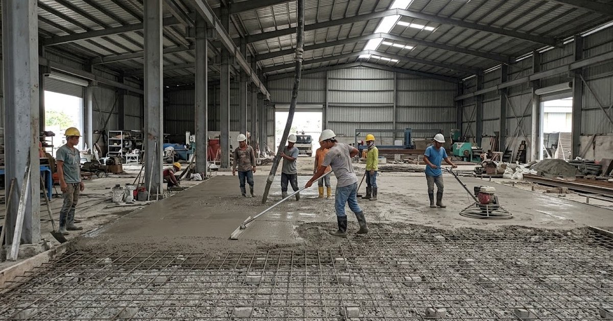 Workers placing and screeding a concrete warehouse floor slab in the Philippines with rebar mesh and a power trowel