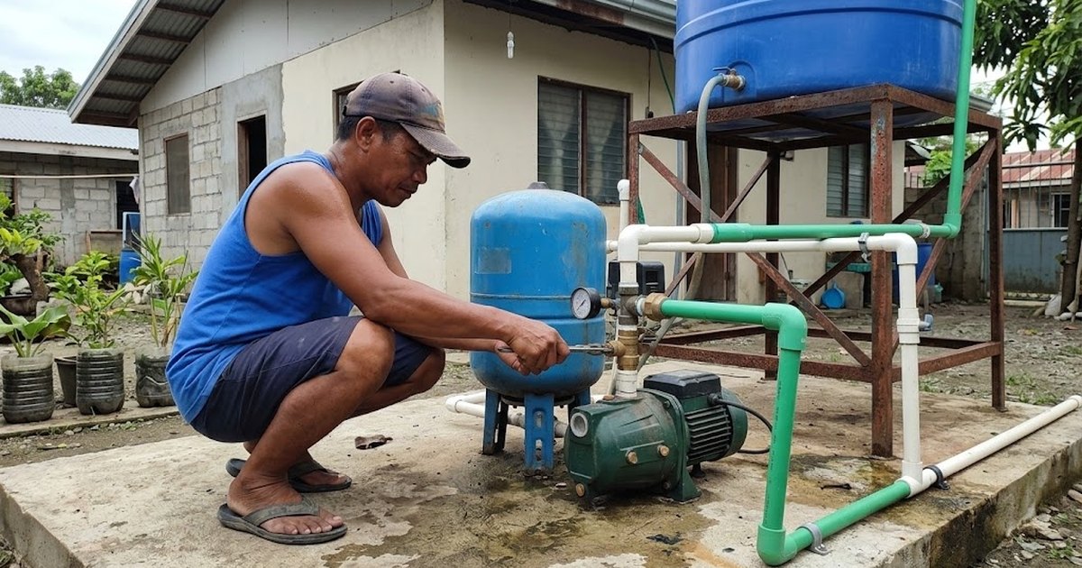 Man adjusting a water pump and pressure tank beside a house
