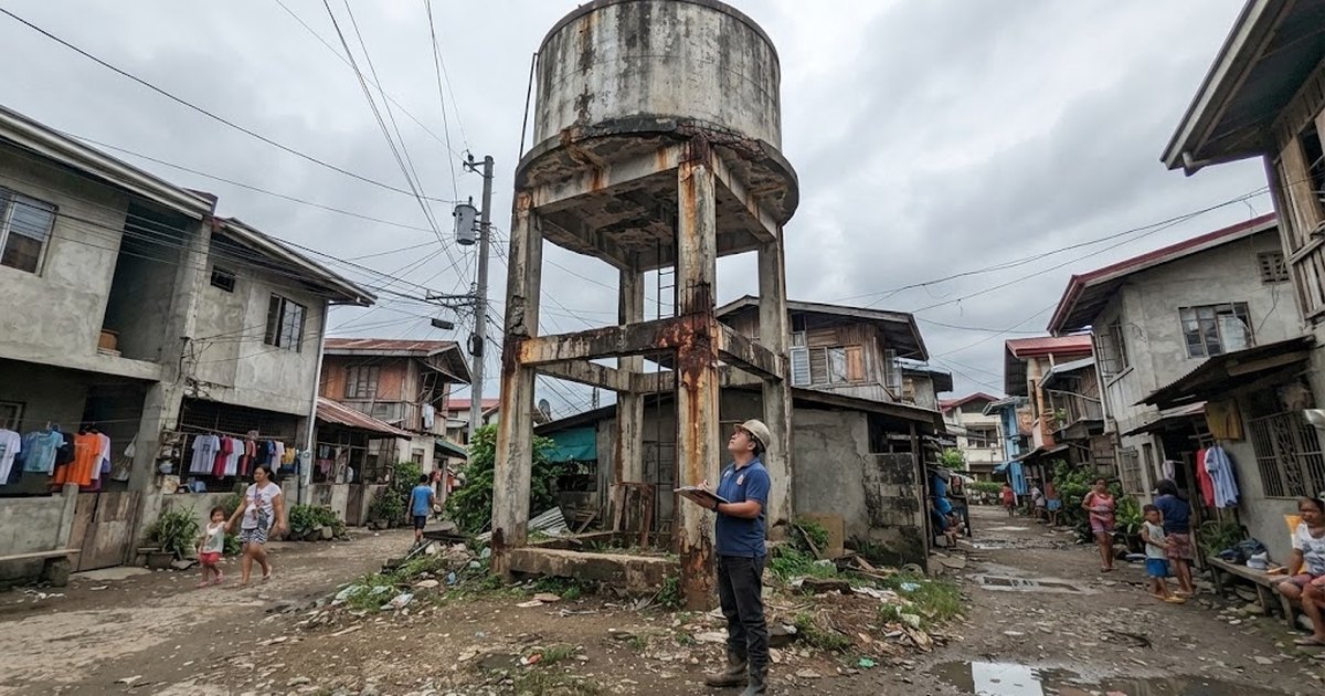 Engineer inspecting an old elevated concrete water tank tower with rust stains and spalled columns