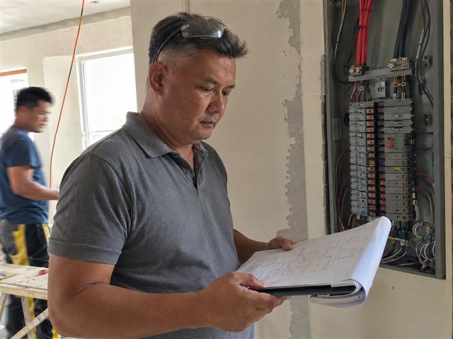 Engineer reviewing a stamped electrical plan next to an open panel board on-site