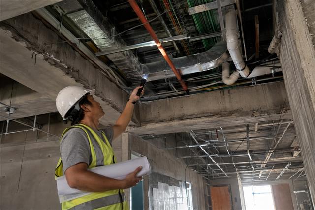 Engineer inspecting coordinated MEPFS ceiling systems — ductwork, conduit, sprinkler and plumbing lines